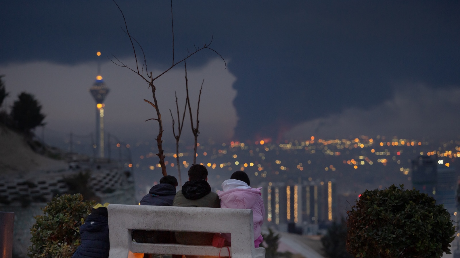 View overlooking Tehran with giant smoke cloud over city with four children on a bench watching the scene. 