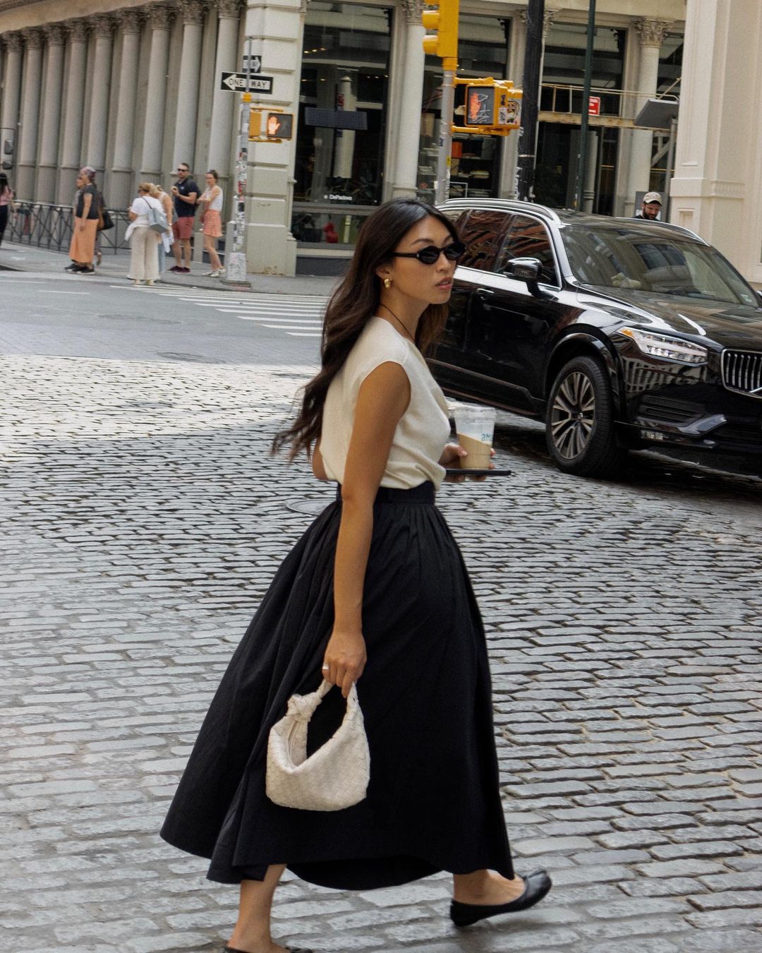 Cotton Skirt Trend: @michellelin.lin wears a black cotton skirt with a cream top whilst walking across a cobble street