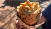 The macaroni cone with goldfish on top in How To Train Your Dragon land at Epic Universe being held in a hand with nail polish on fingers.