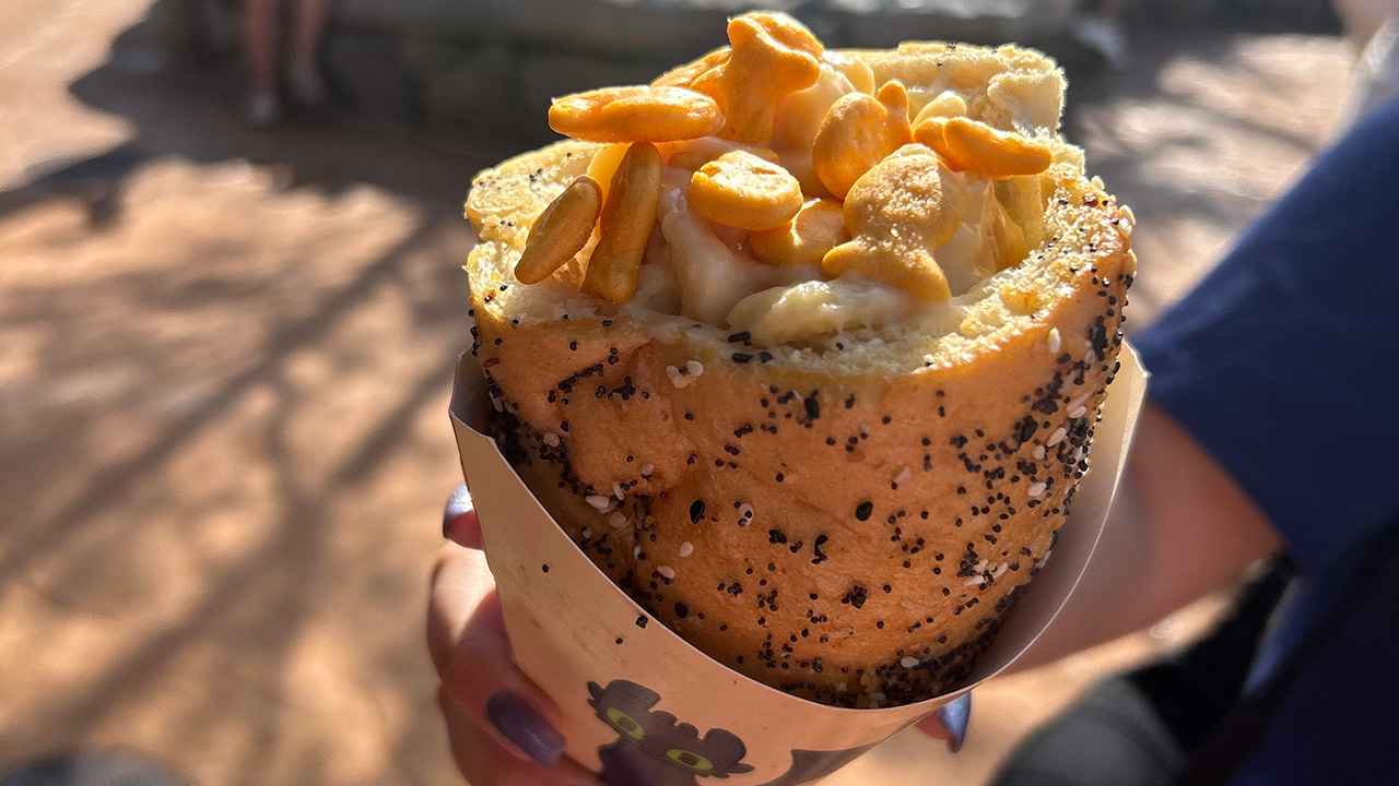The macaroni cone with goldfish on top in How To Train Your Dragon land at Epic Universe being held in a hand with nail polish on fingers.