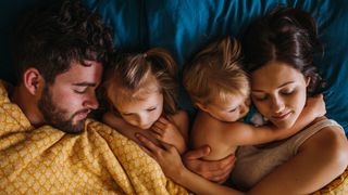 A family sleeps in bed together, though the two children are both awake.