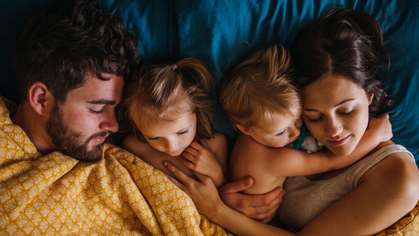 A family sleeps in bed together, though the two children are both awake.