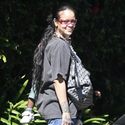 Rihanna was seen enjoying a stroll with her son RZA in Beverly Hills, dressed in a laid-back outfit featuring an oversized gray graphic t-shirt and loose blue jeans with very strategic bag placement covering her belly amid pregnancy rumors. She accessorized with a designer bag and bold black-and-white spiked sneakers, adding pink-tinted sunglasses for a pop of color. Shot on 04/21/25