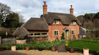 a cosy thatched cottage exterior with an immaculate garden and plant pots on the gravel driveway