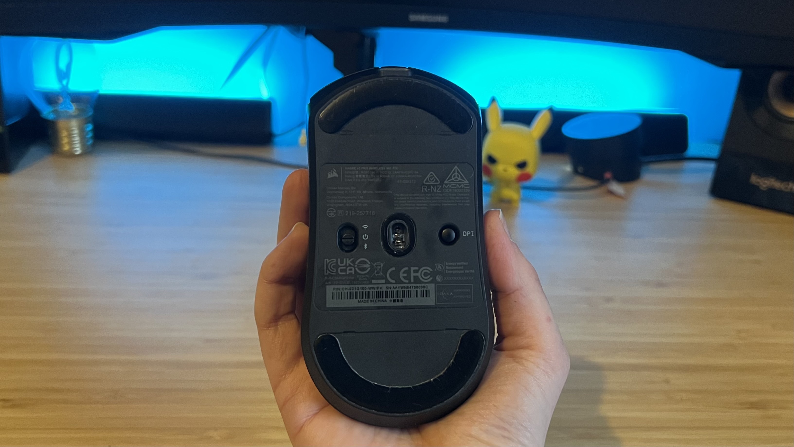 Hand holding Corsair Sabre V2 Pro Wireless MG gaming mouse with its sensor and controls facing the camera