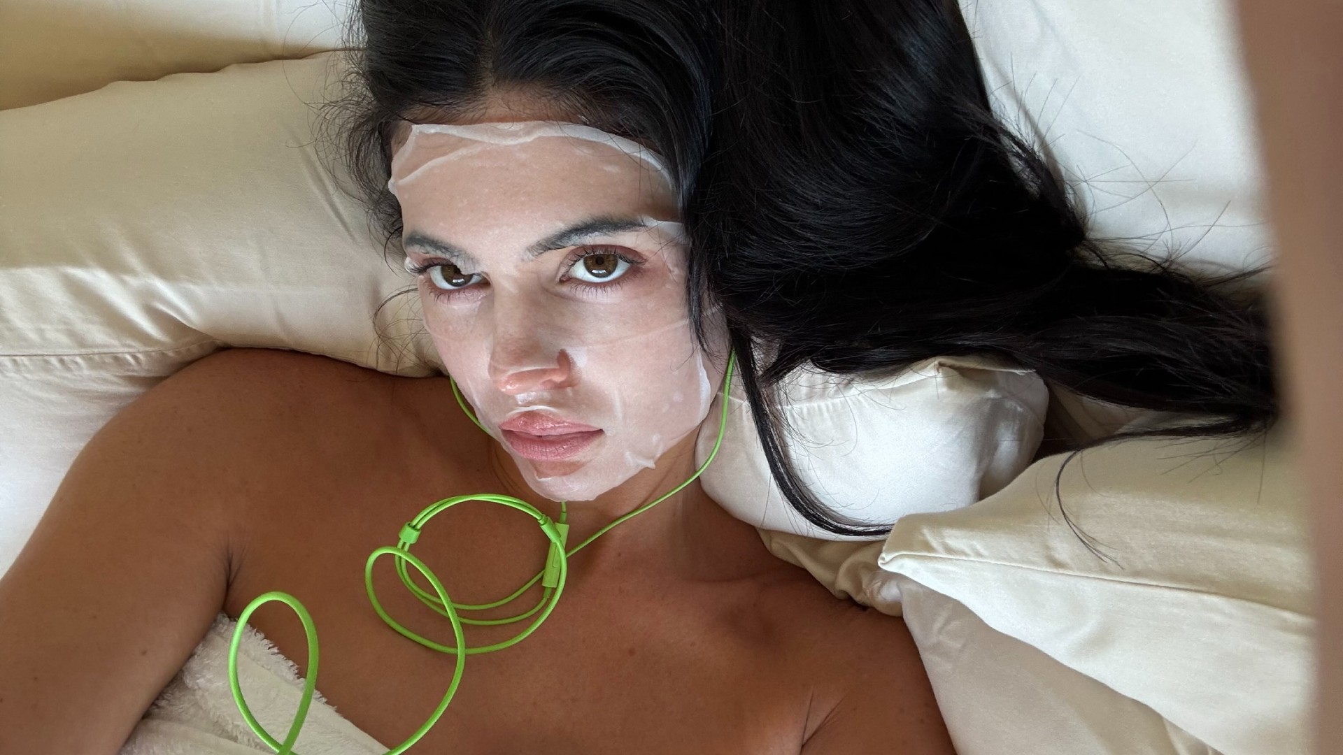 Selfie of Kylie Jenner wearing a sheet mask and green headphones