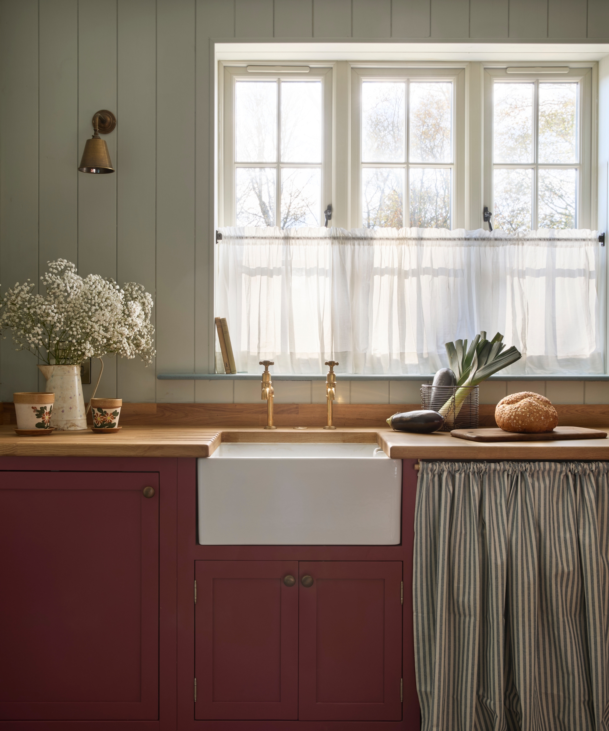 A coastal cottage kitchen with light blue paneled walls, wood countertops, and burgundy cabinets