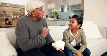 a grandfather and his granddaughter holding a piggy bank talking about finances