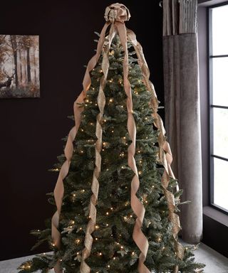 A gold bow tree topper with long ribbons on artificial Christmas tree