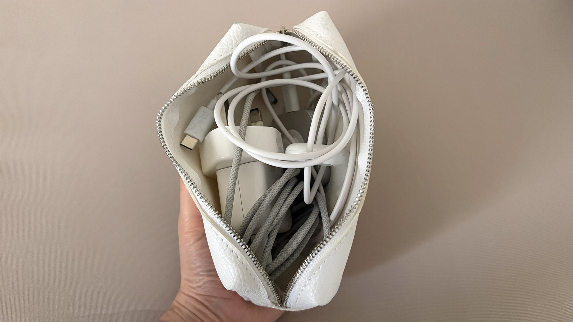 A close up of a hand holding an open pouch filled with cables and chargers