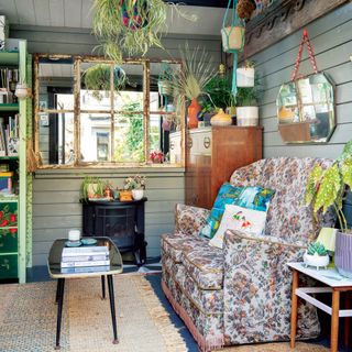 Garden office with vintage sofa, wall panelling, window mirror, log burner and hanging planters