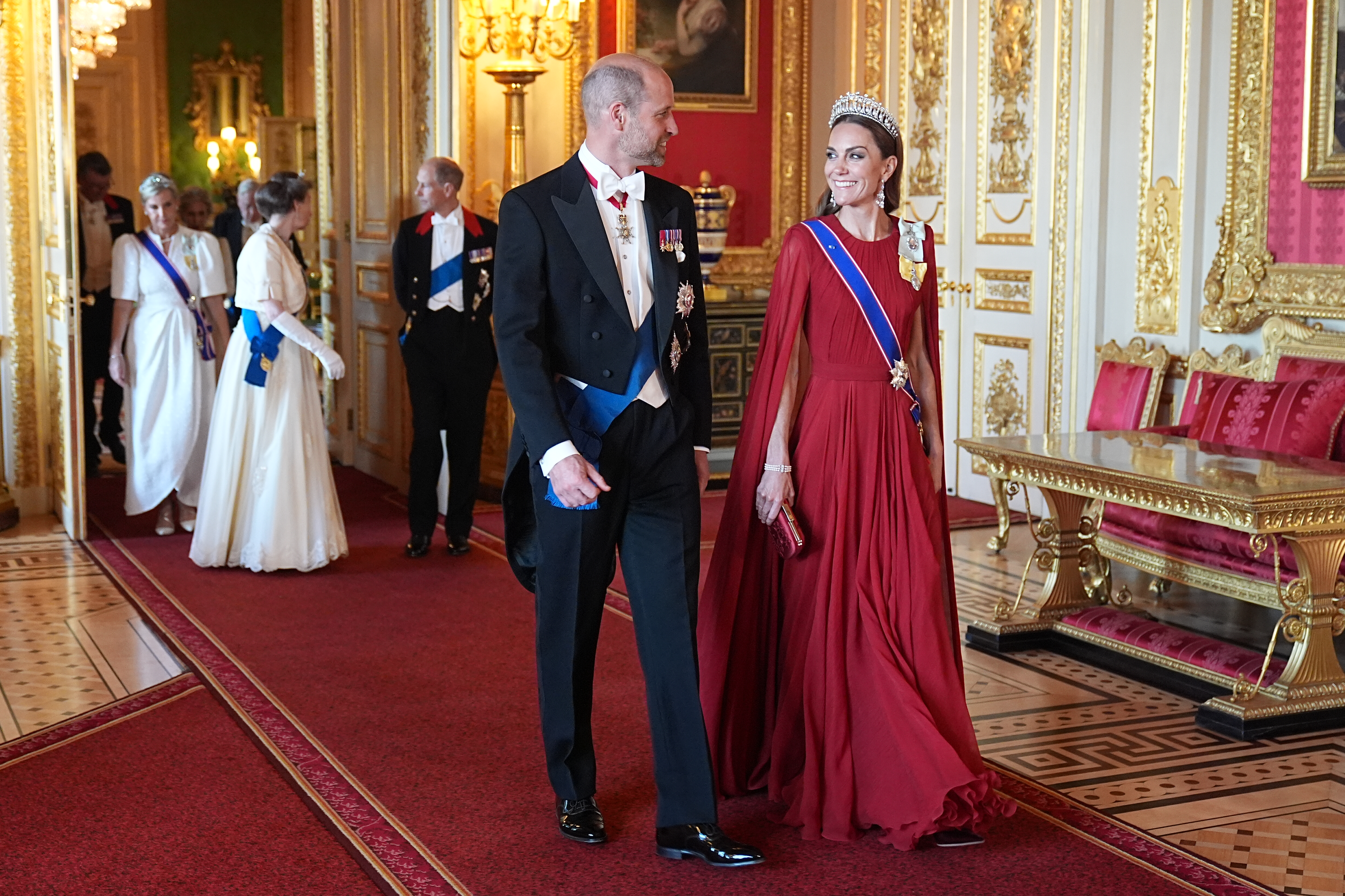 Princess Kate in a red gown and tiara walking with Prince William, with Princess Anne, Prince Edward and Duchess Sophie behind them at Windsor Castle
