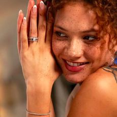 A woman facing the camera while modelling a silver diamond ring and bracelet with her hand by her face