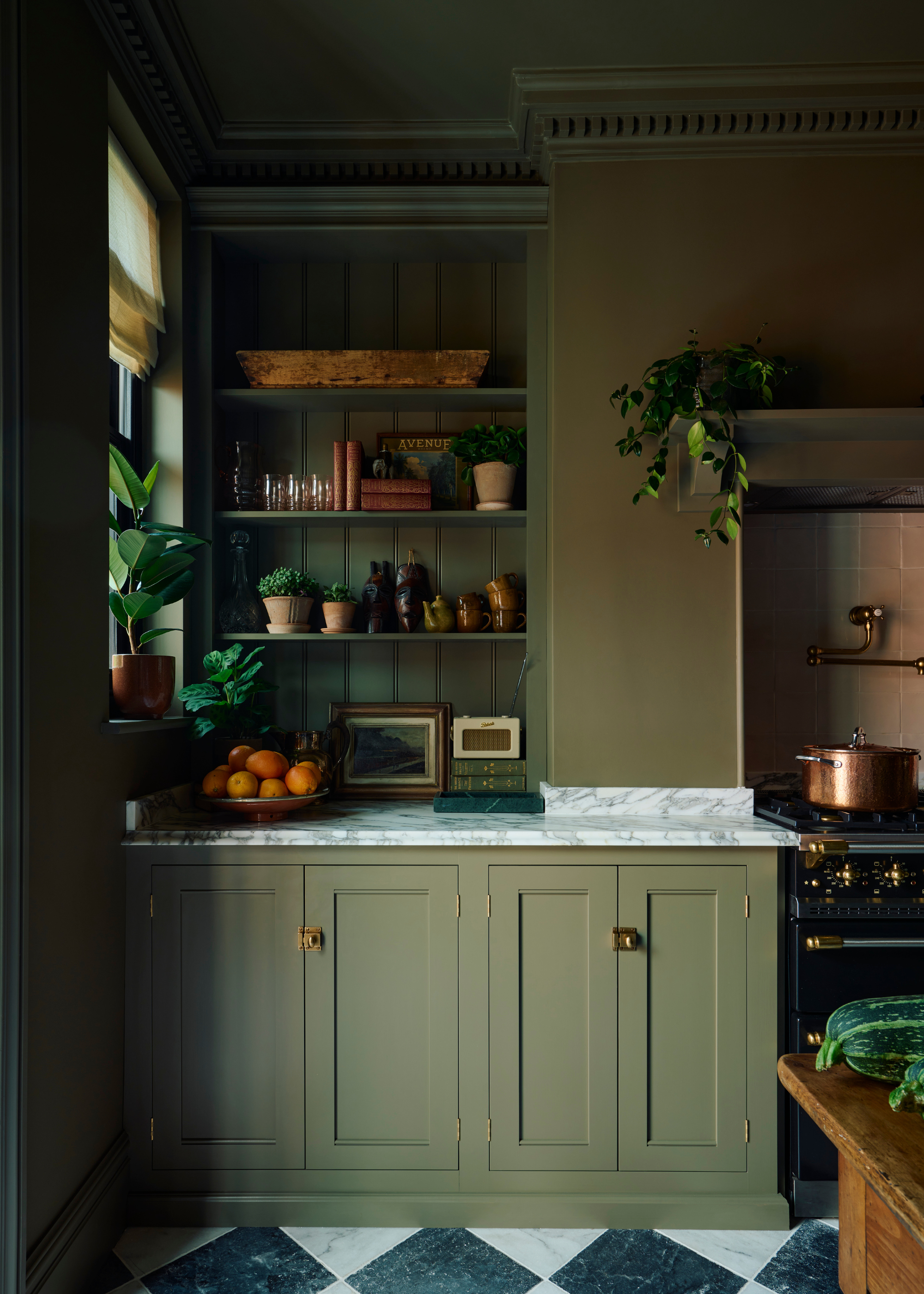 A dark olive green color-drenched traditional kitchen with black and white chequerboard flooring and terracotta styling