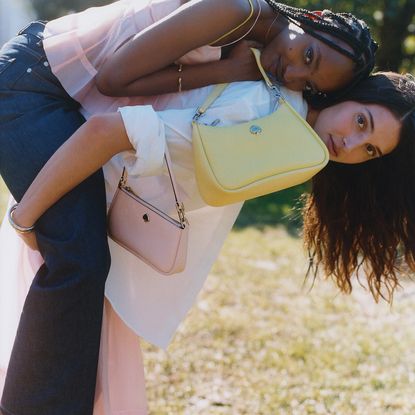 Two models giving eachother a piggyback wearing pastel pink and yellow Kate Spade handbags