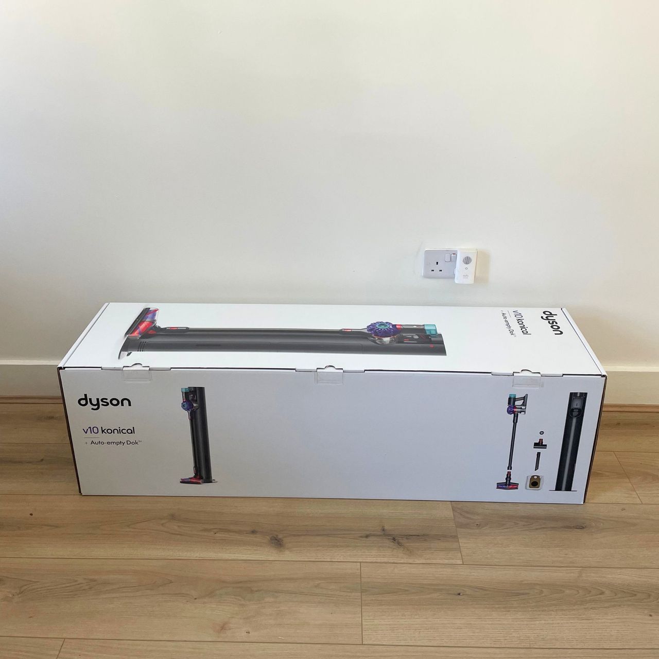 Dyson V10 Konical Cordless Vacuum and Auto-Empty Dok branded box sitting on wood-effect flooring in front of a white wall