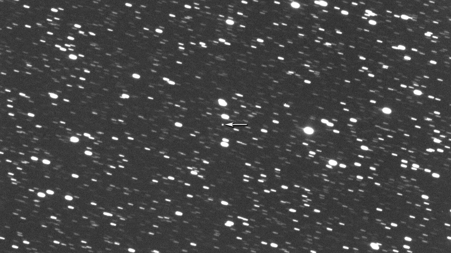 The potentially hazardous asteroid 612356 2002 JX8 is pictured against a field of blurry white stars, with its location highlighted with a white arrow.