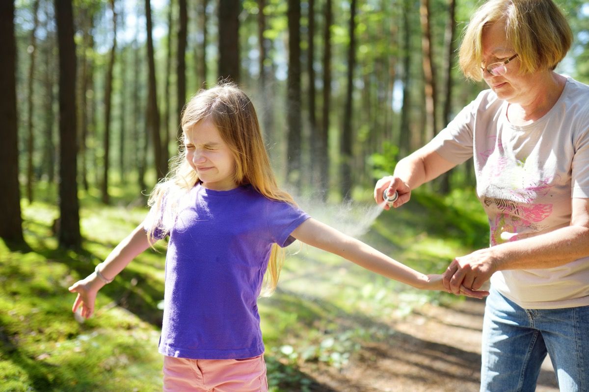 Woman spraying bug spray on daughter.