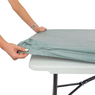 green elastic tablecloth being fitted over a white plastic picnic table