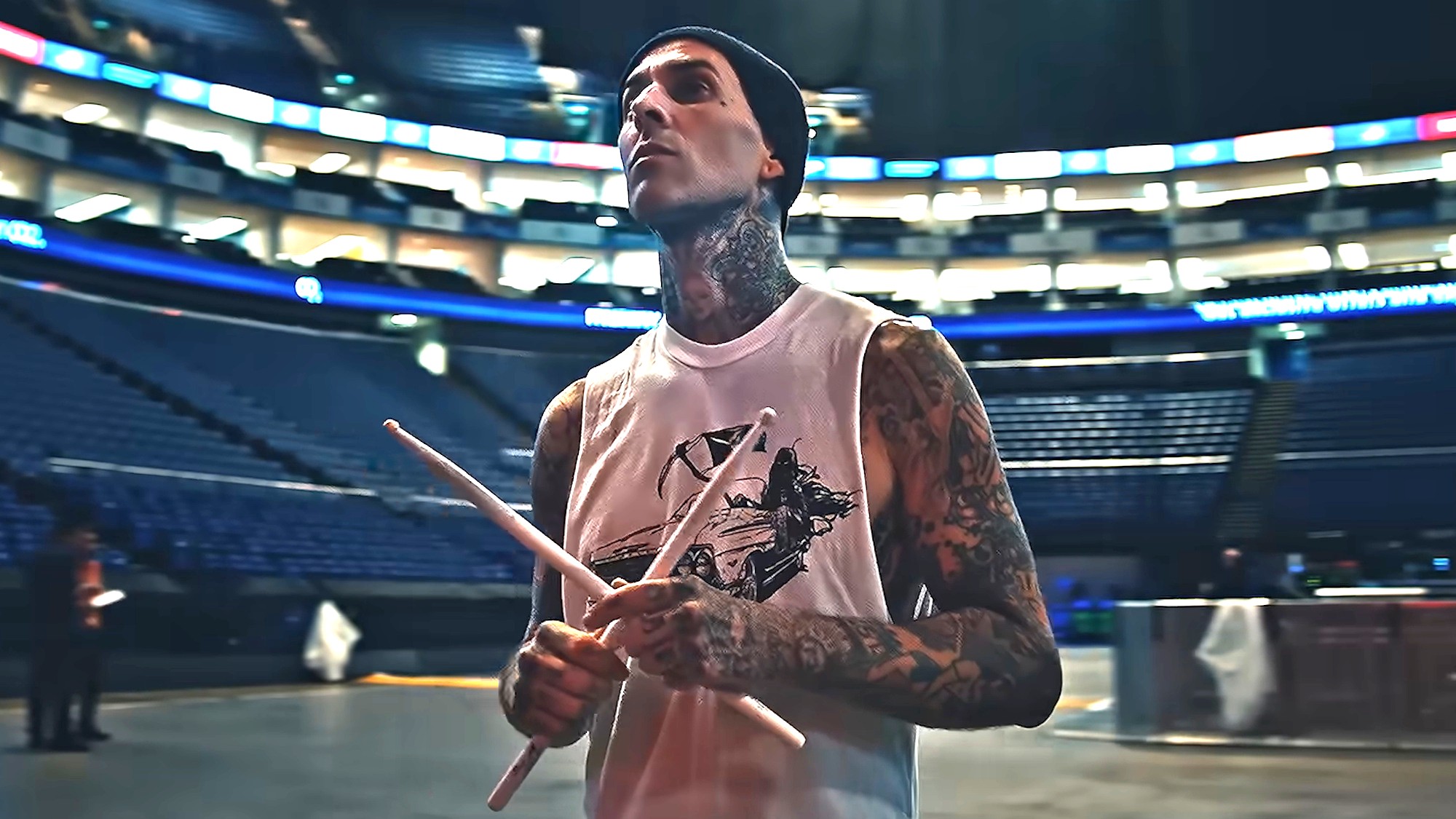 Travis Barker is shown holding drum sticks in an empty arena in the Hulu documentary Travis Barker: Louder Than Fear.