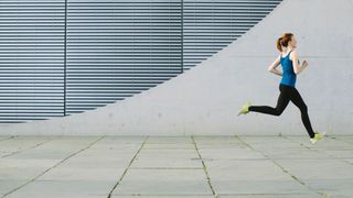 Woman running along industrial front in workout clothes and running trainers
