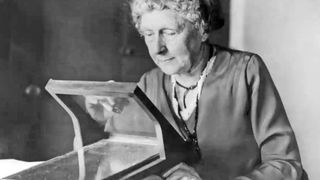 Black and white photo of American astronomer and suffragist, Annie Jump Cannon. She is sitting at a desk, carefully looking a spectroscope as she works on classifying stars.