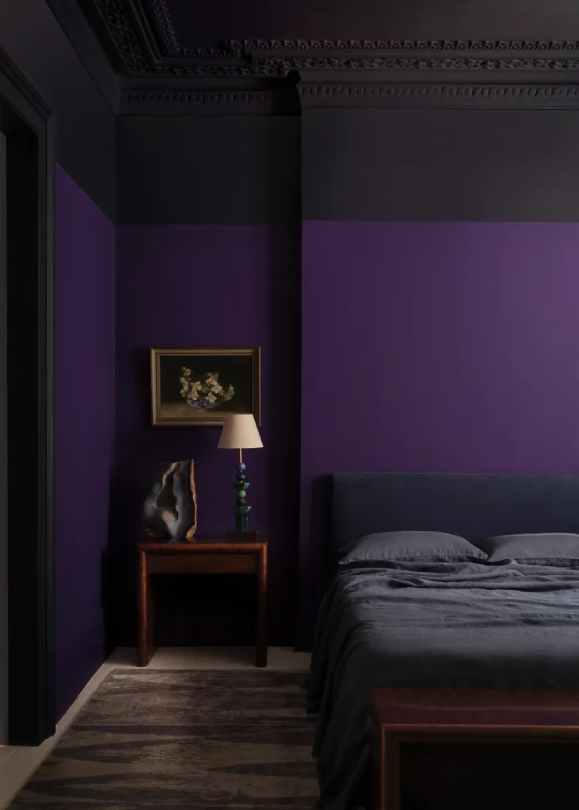 An amethyst purple bedroom with a geode and a lamp on the side table