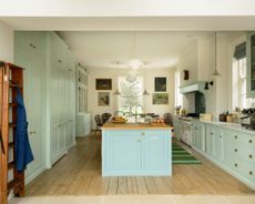 pale blue and off white kitchen with custom cabinetry, large kitchen island with wooden countertop and sink, wooden floorboards, ladder, artwork, view of kitchen table at far end, rug, white oven