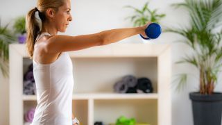 Woman performs alternating front raise shoulder exercise with dumbbells