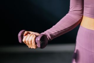 A women wearing a purple activewear set holding a matching small, purple dumbell.