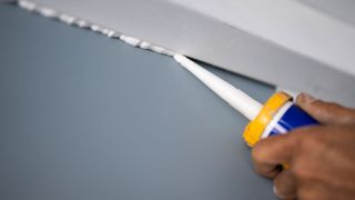 Caulking gun applying white silicone to wall