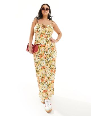 model wears floral dress with ruching and sneakers with a red handbag