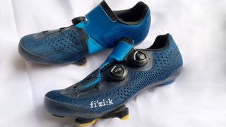 A pair of Fizik Infinito R1 Knit shoes in blue lying upon a white cloth