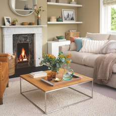 Wood coffee table in neutral living room. It has a tray with water jug and two cups, fresh flowers and books