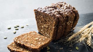Wholegrain bread loaf sitting on slate worktop surrounded by pumpkin seeds