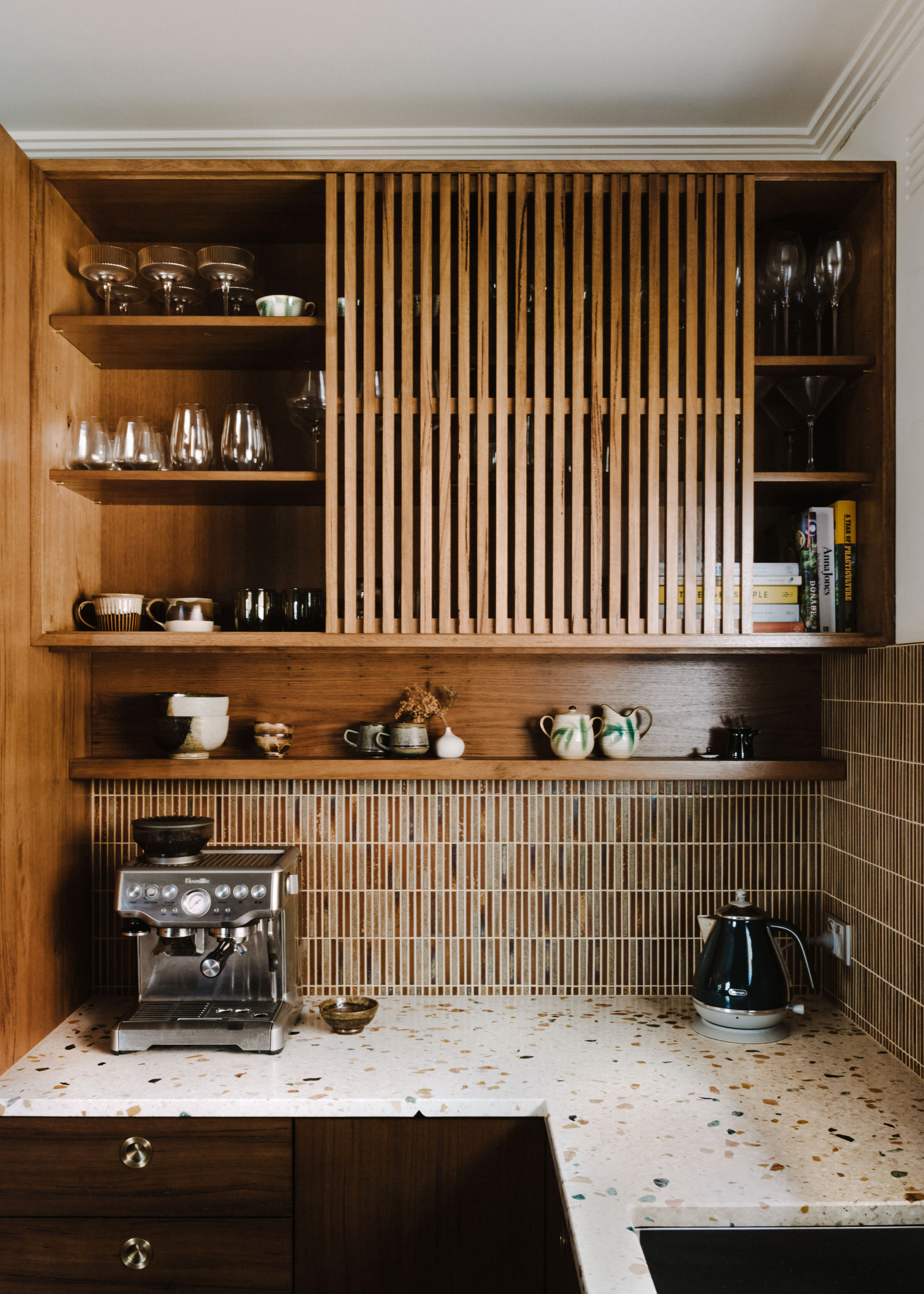 A Japanese modernist kitchen with wood open shelving, brown kit-kat tiles and a white terrazzo worktop with flecks of brown