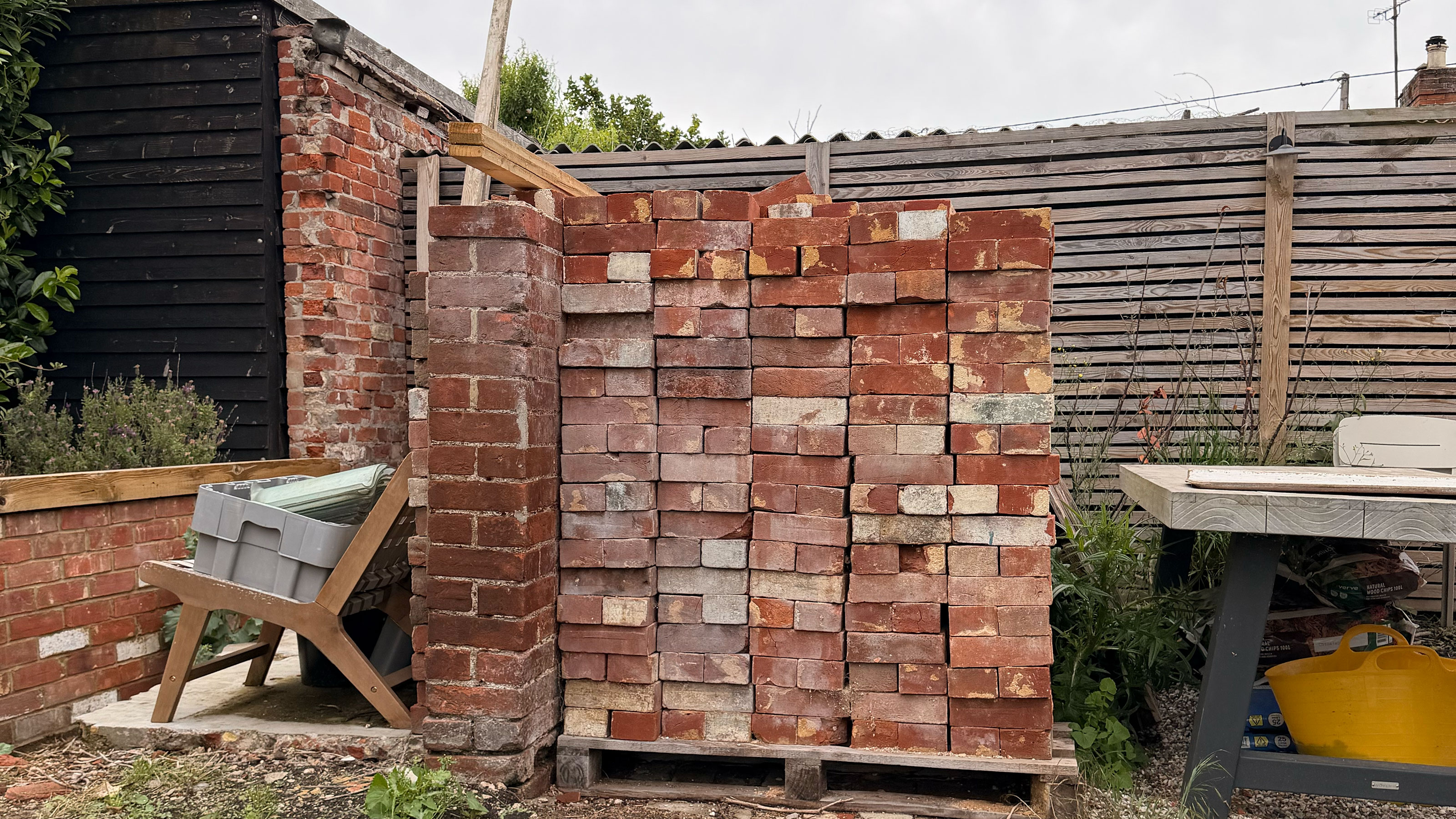 Large piles of bricks in front of slatted wooden fence in garden 