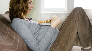 A pregnant woman sitting on a couch with her feet propped up and a plate of food resting on her belly