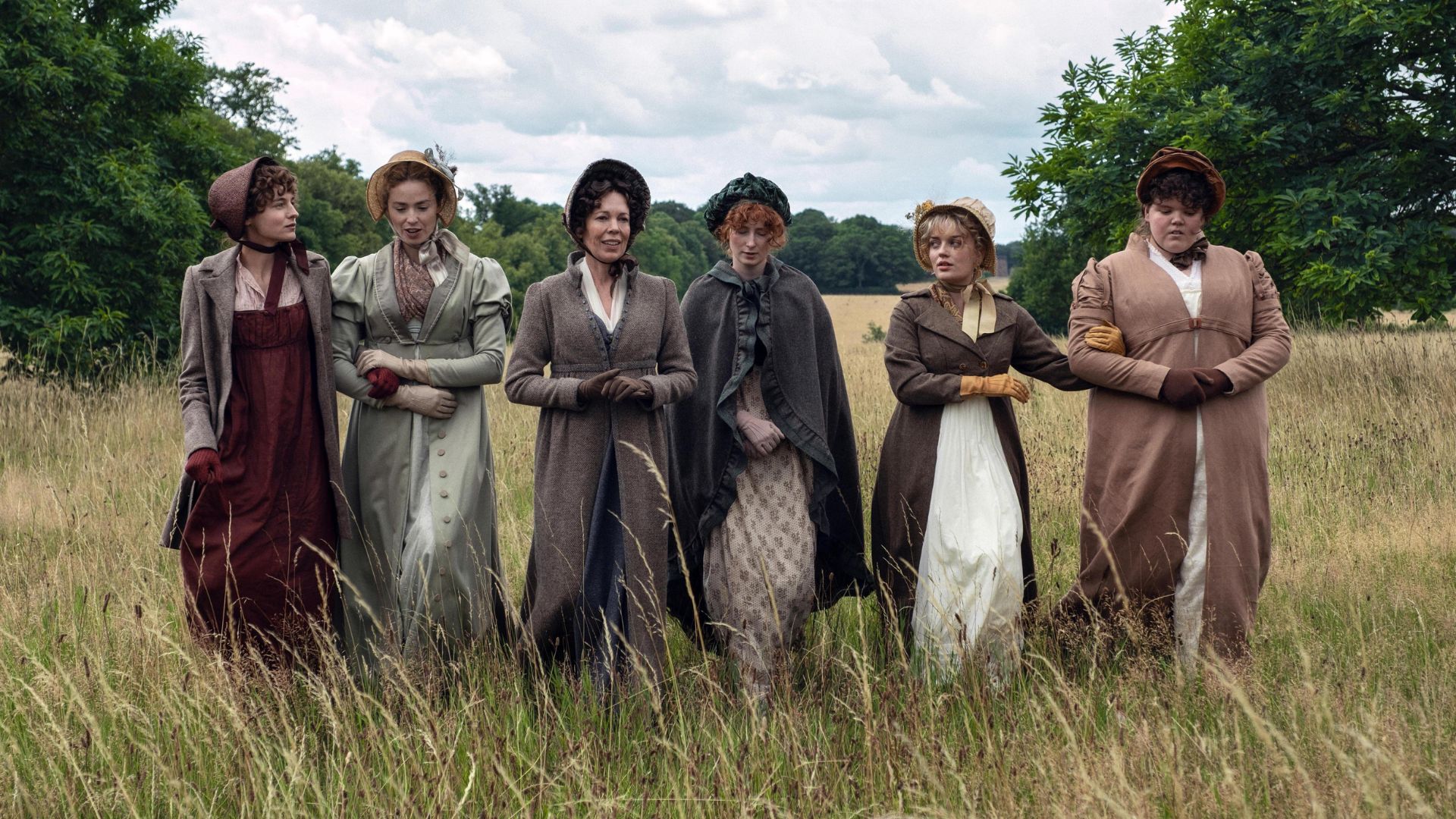 The Bennet women walk in a line through a field with their arms linked