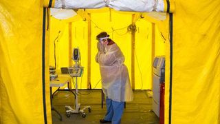 A nurse practitioner puts on protective gear in a tent before testing a possible Coronavirus patient in Newton, MA.
