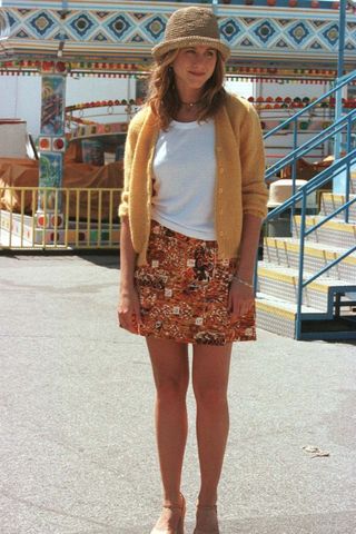 Jennifer Aniston in the 90s wearing a printed skirt, yellow cardigan and bucket hat