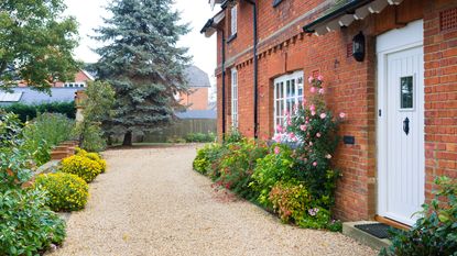 gravel driveway with plants in borders around red brick house with white door