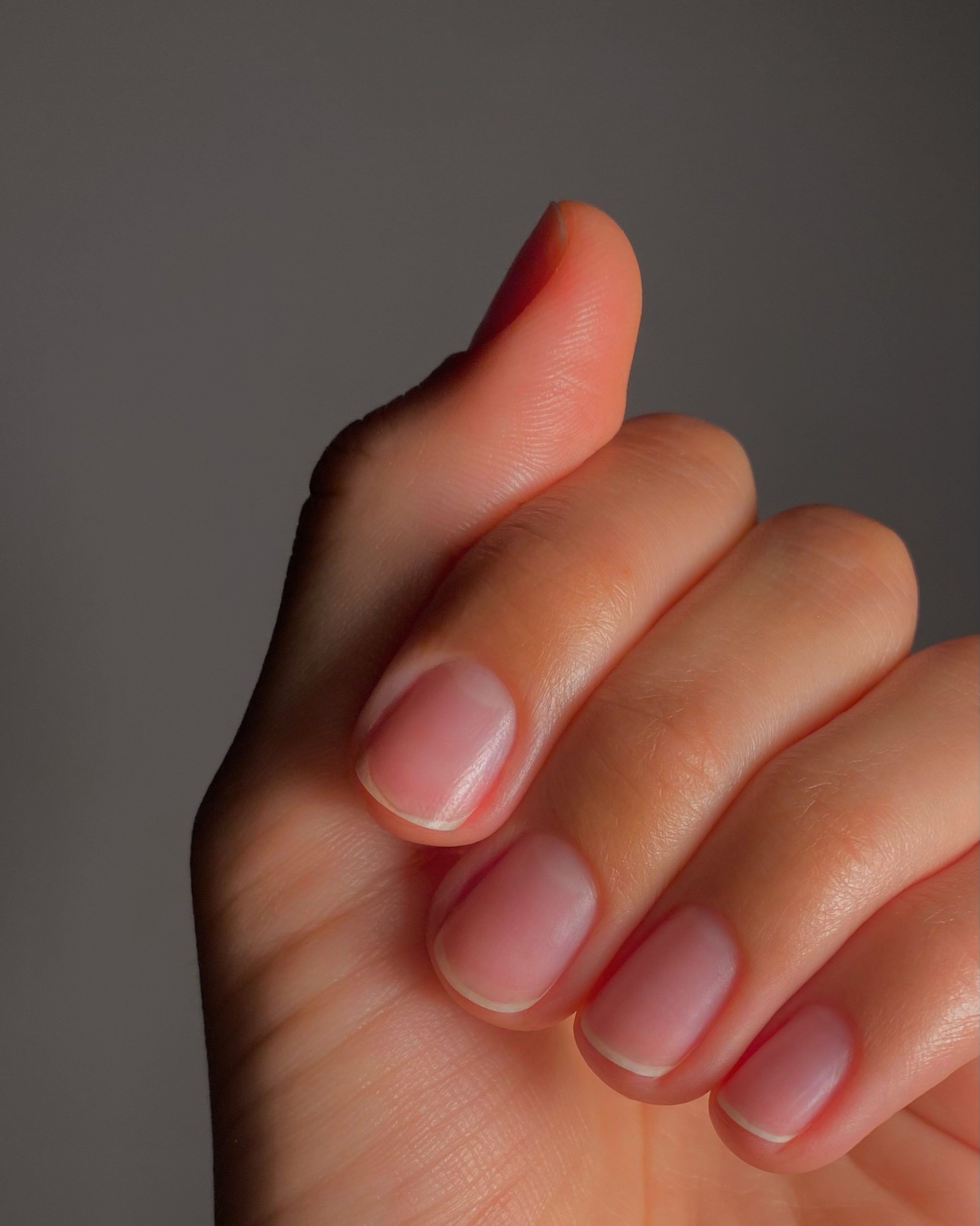 a hand over a grey background with freshly manicured, bare nails in a squoval shape