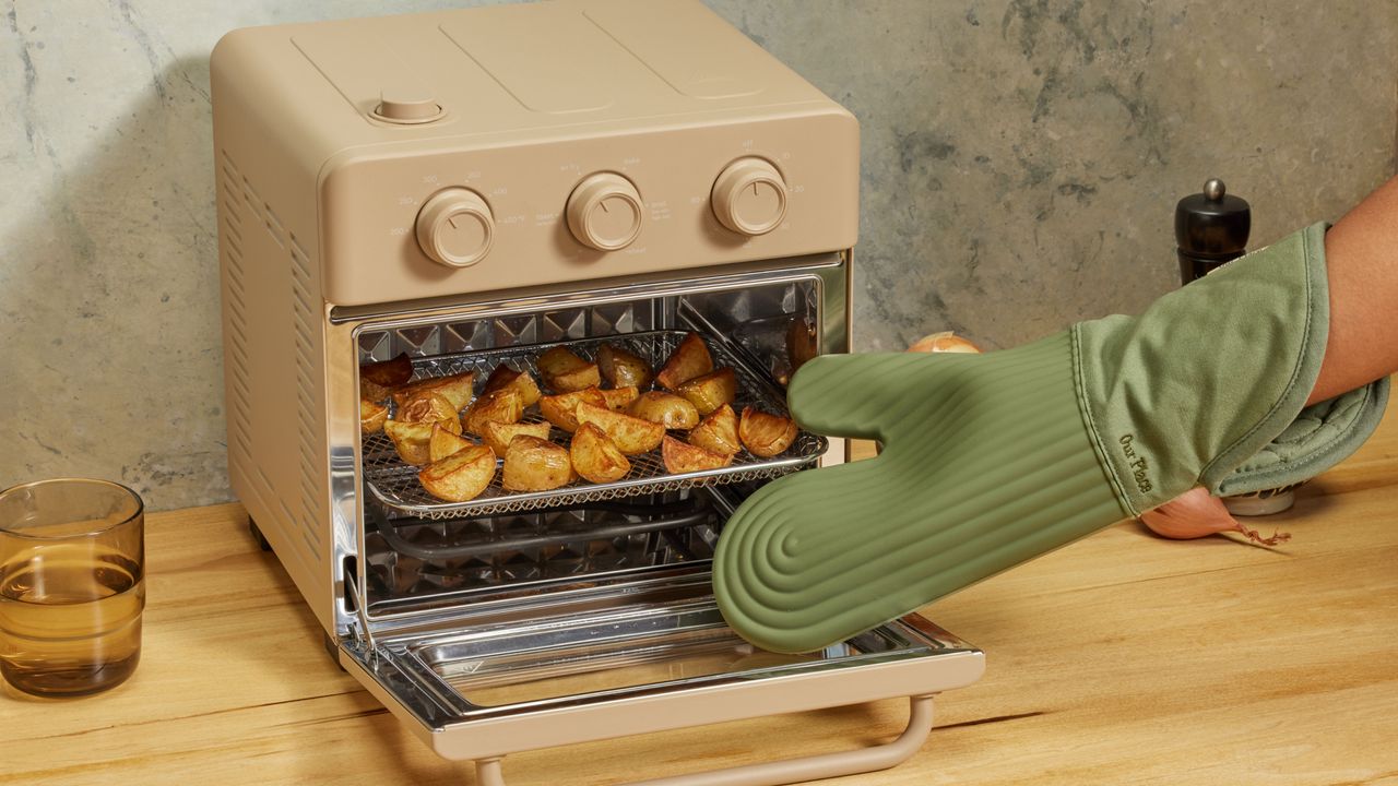 Sage green oven glove taking tray out of small oven