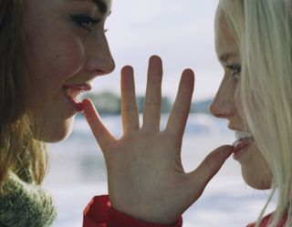 Two woman facing each other with a splayed hand between their faces and their tongues out.