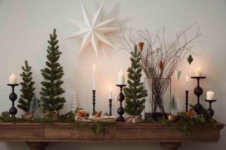 row of table top Christmas trees with candles, vase and decorations on a console