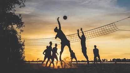 people playing volleyball on the beach at sunset