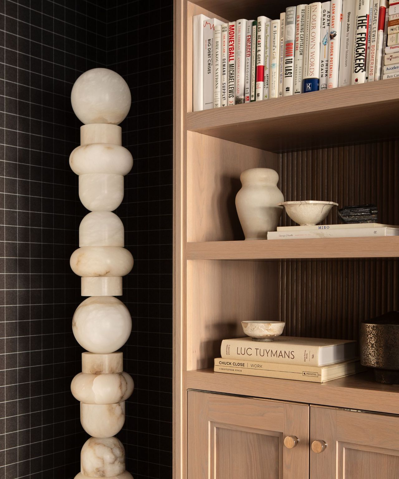 A wooden shelving unit with books and decorative objects, and a tall sculpture in the corner