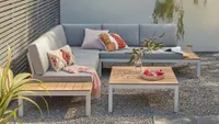 A wooden outdoor corner sofa with grey cushions
