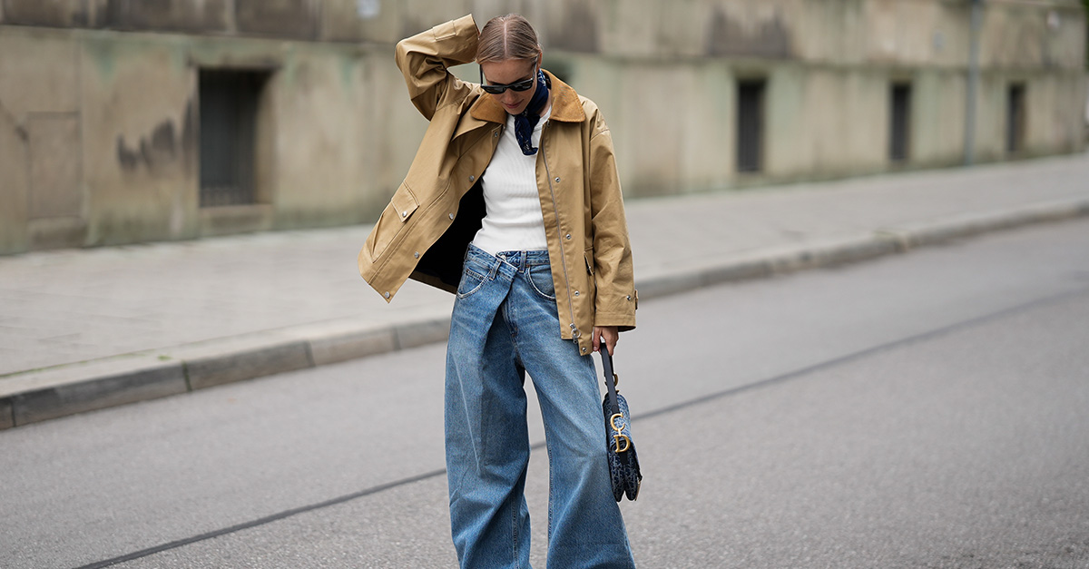 Woman wearing jeans, a white tee, and a tan chore jacket. 